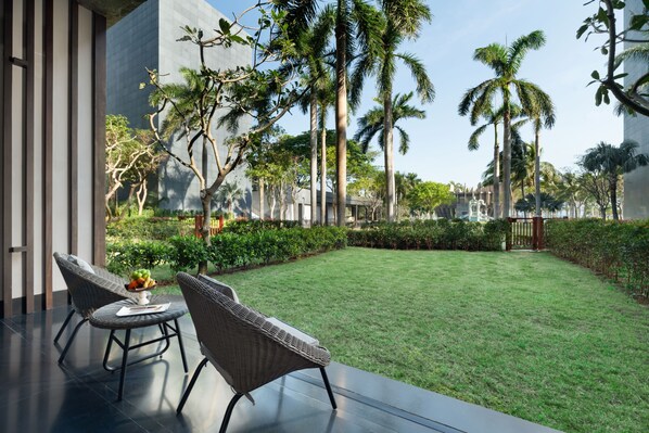 A patio with wicker furniture, a grassy lawn, and tall palm trees.
