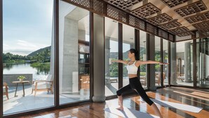 A spacious room with large windows overlooking a lake, wooden flooring, and yoga mats.