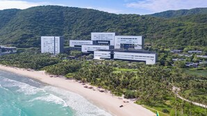 A coastal hotel with multiple buildings, a beach, and a mountainous backdrop.