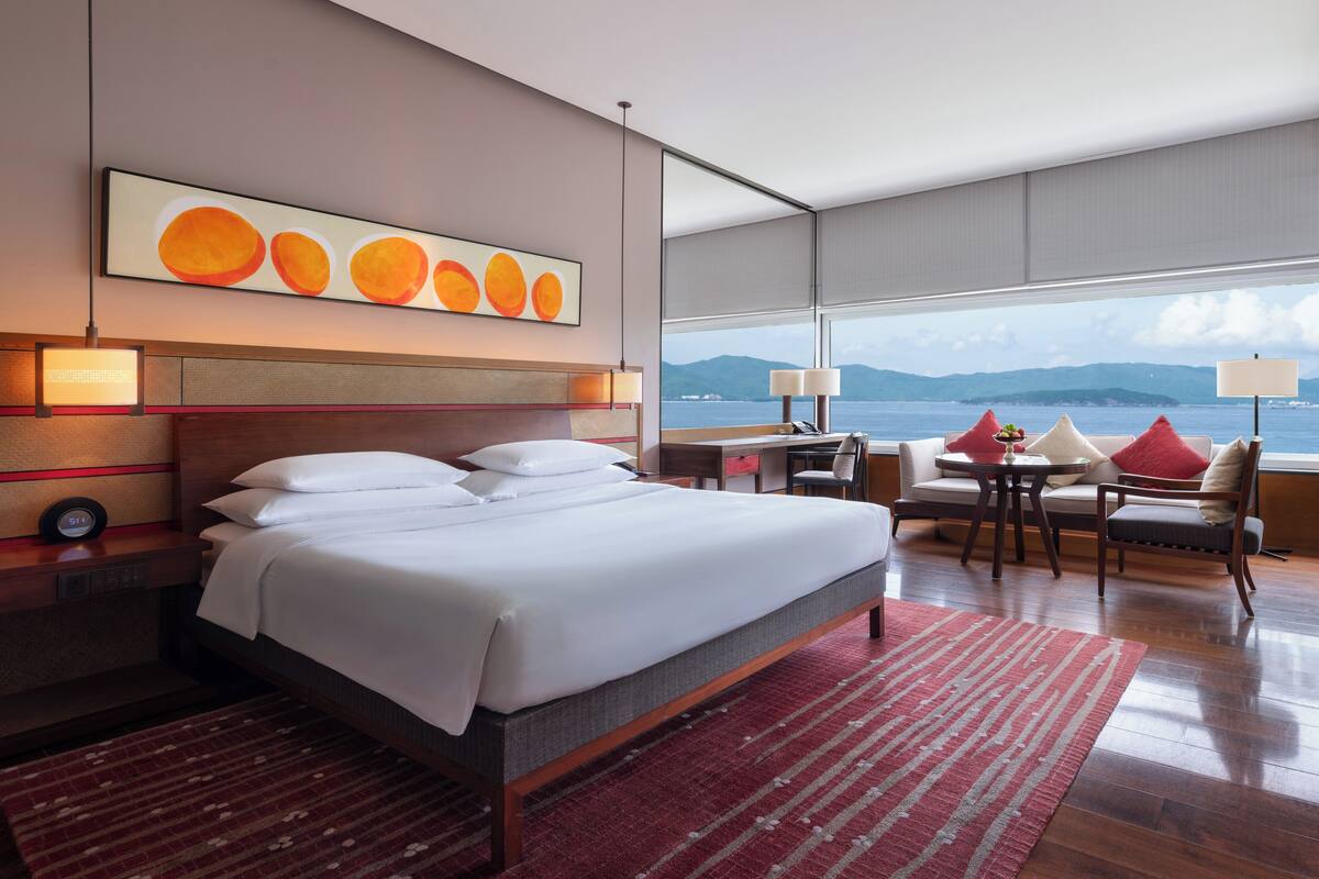 A modern hotel room with a large bed, a desk, and a view of the sea.