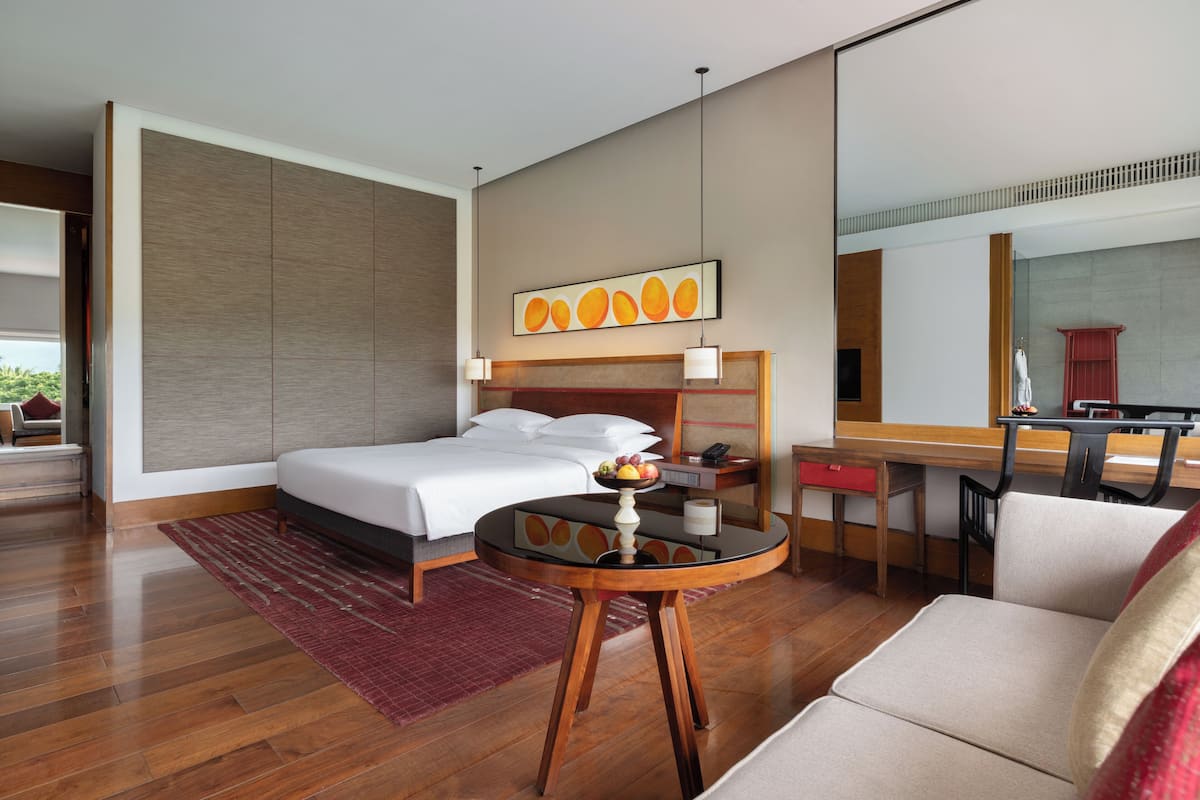 A modern hotel room with a large bed, a desk, a chair, and a dining table with fruit.