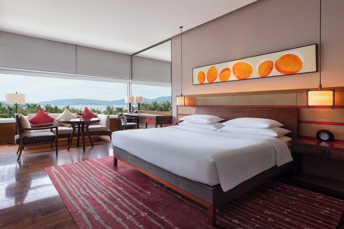 A modern hotel room with a large bed, a desk, a chair, and a view of the mountains.
