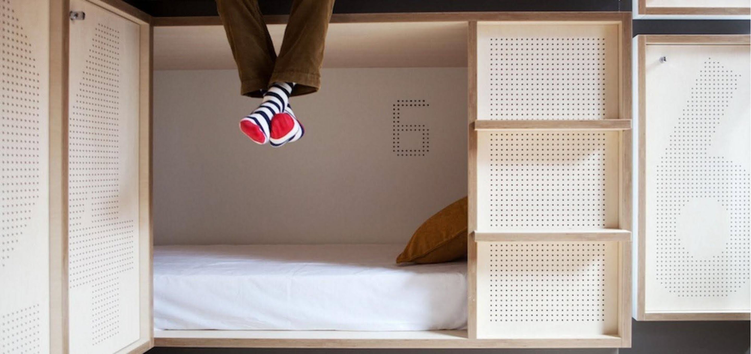A bunk bed with a white mattress, a brown pillow, and a person wearing striped socks and brown pants.