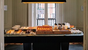 Un bufé de desayuno con diversos pasteles y bebidas, frente a una ventana con vistas a edificios.