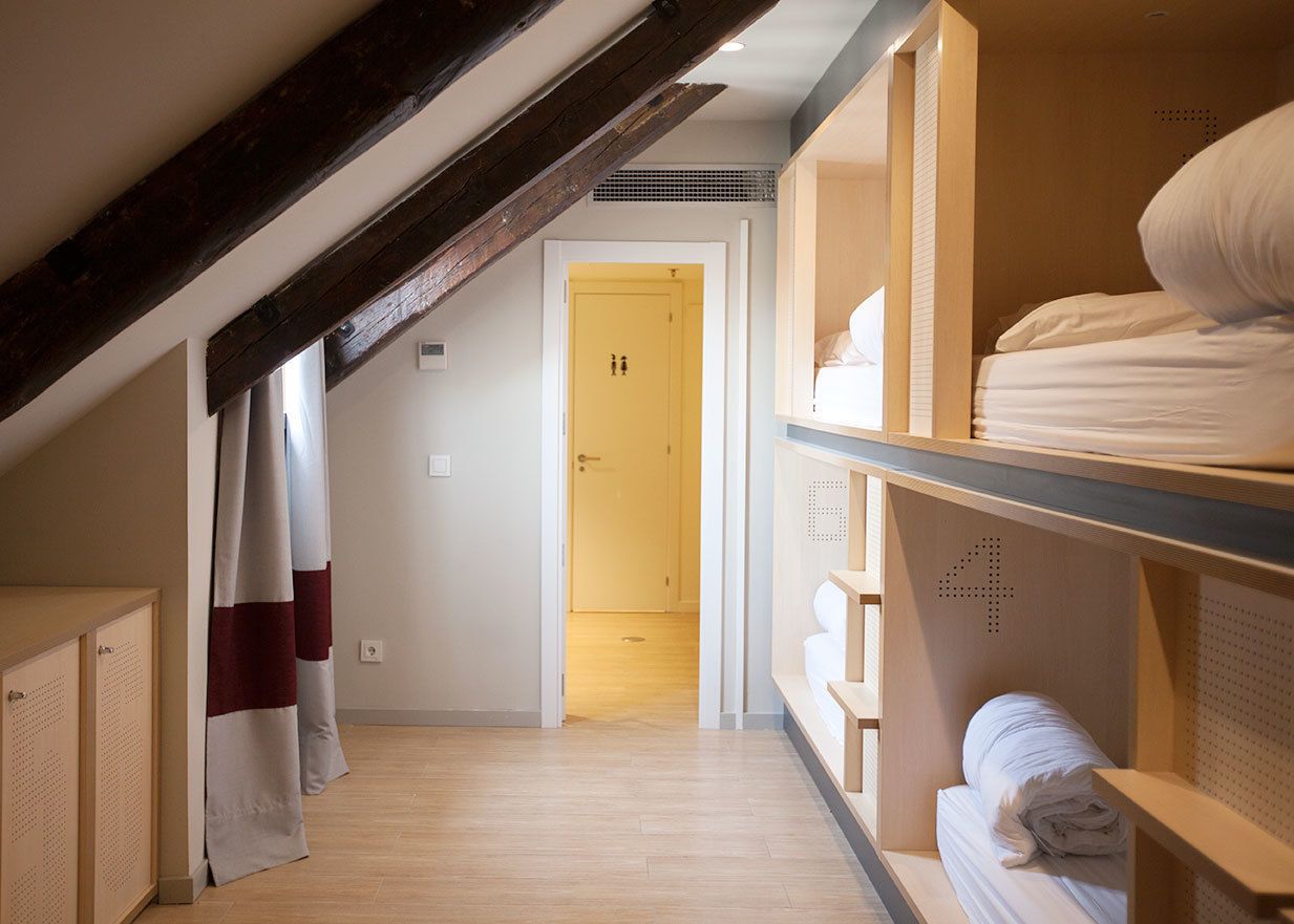 A hotel room with a sloped ceiling, wooden beams, a bed with white bedding, and a wooden wardrobe.