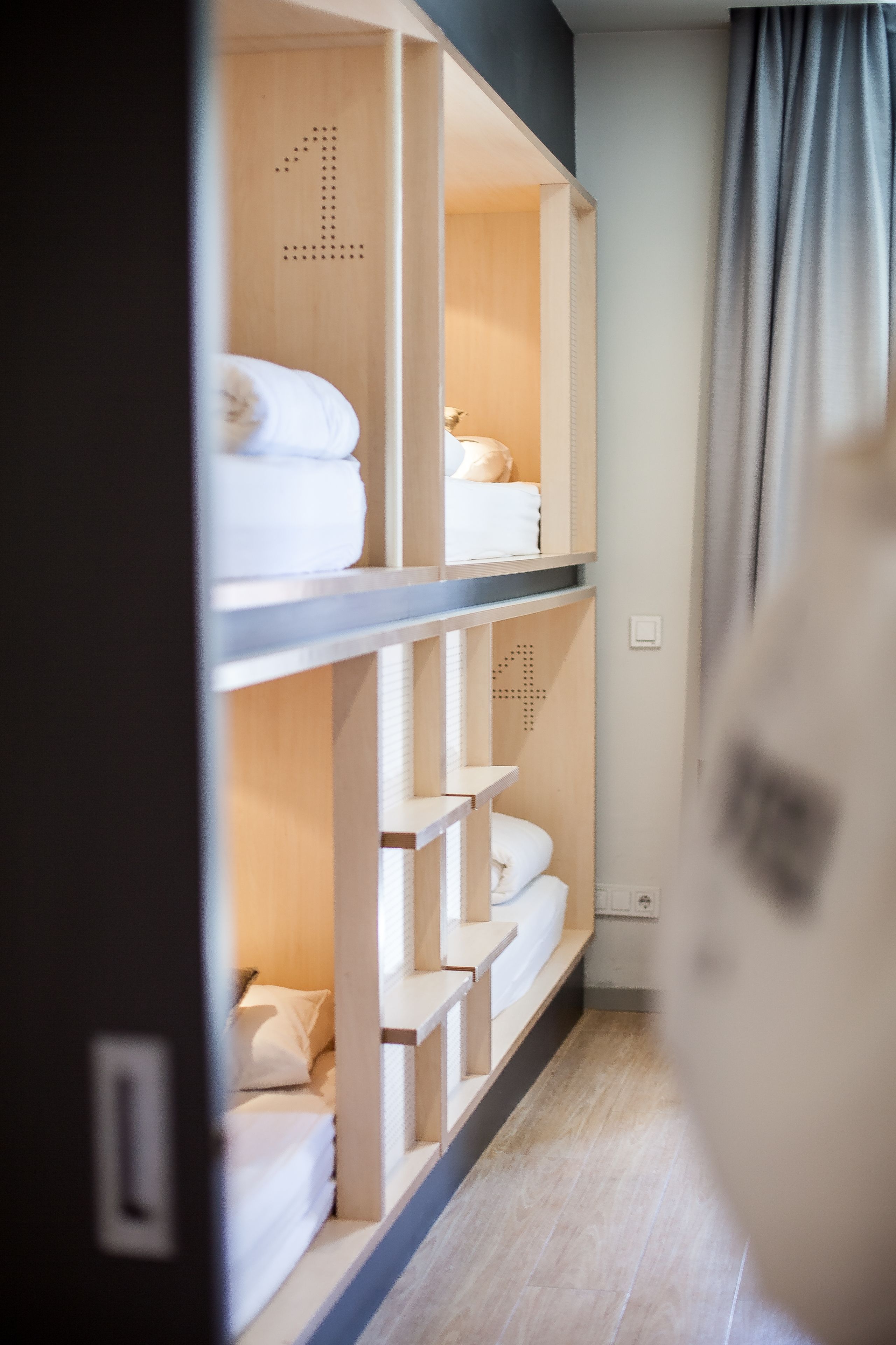 A hotel room with a wooden wardrobe containing neatly folded towels and a bed with a white pillow.