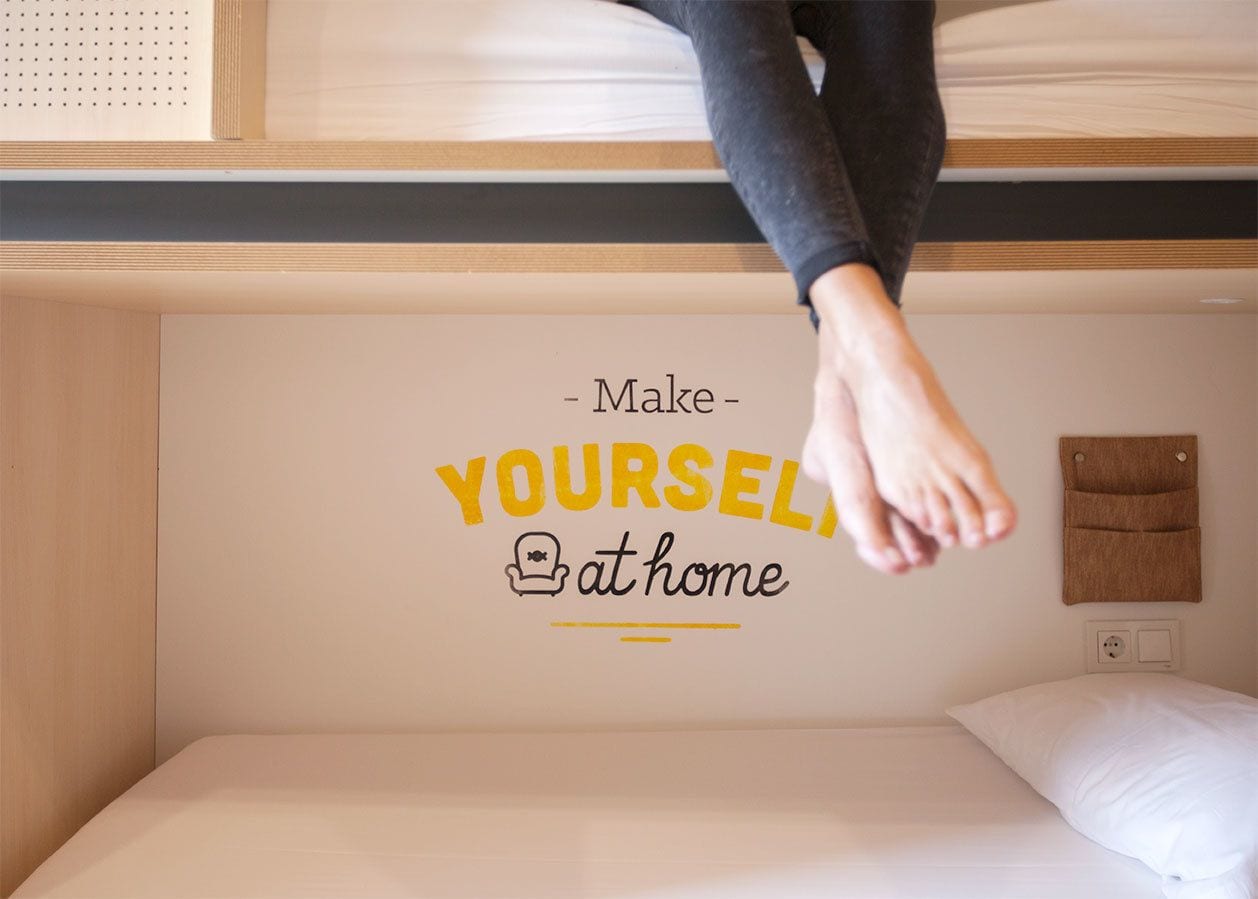 A bed with a wall decal that reads "Make YOURSELF at home".