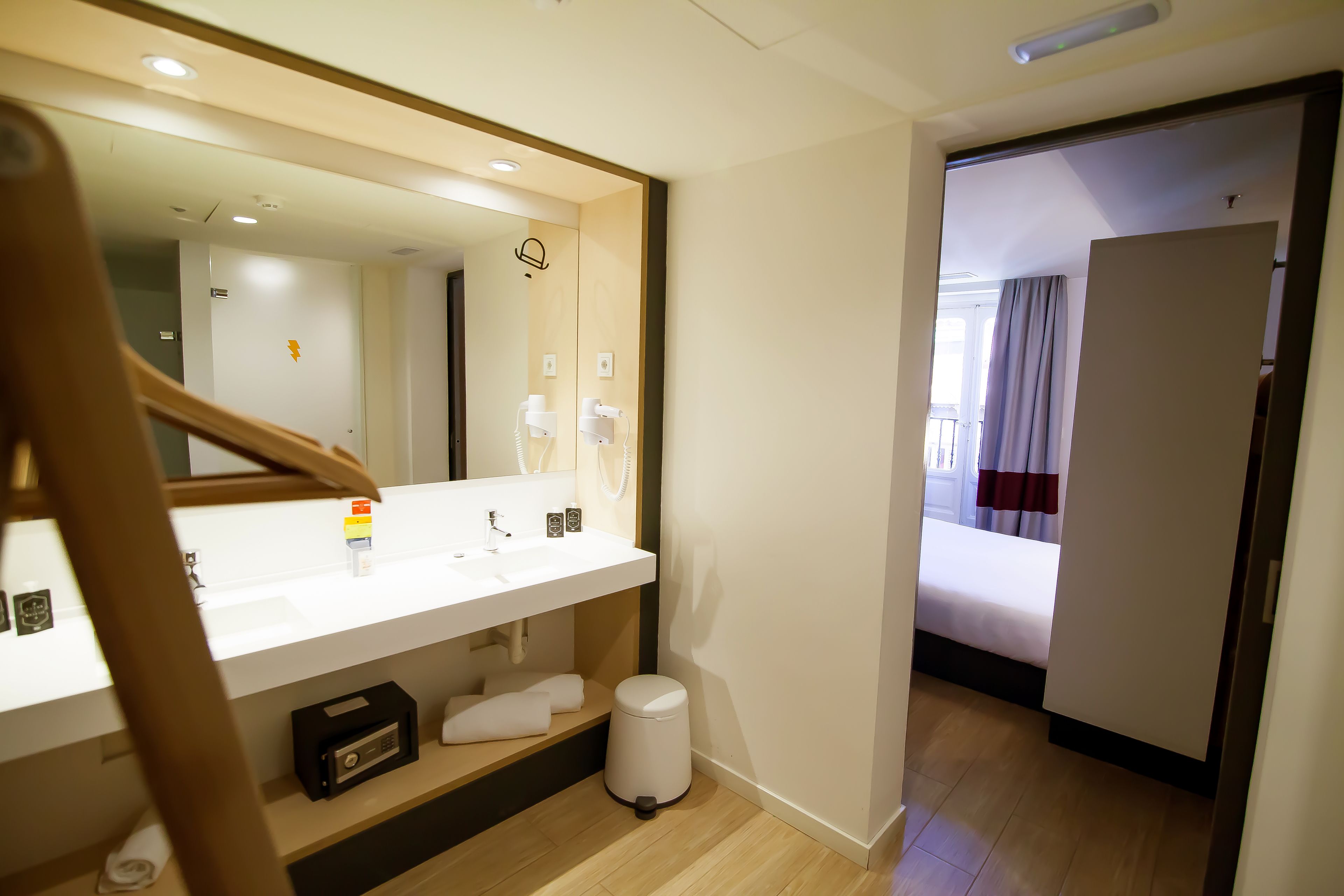 Une salle de bain d’hôtel avec un grand miroir, un lavabo, un porte-serviettes et une poubelle.