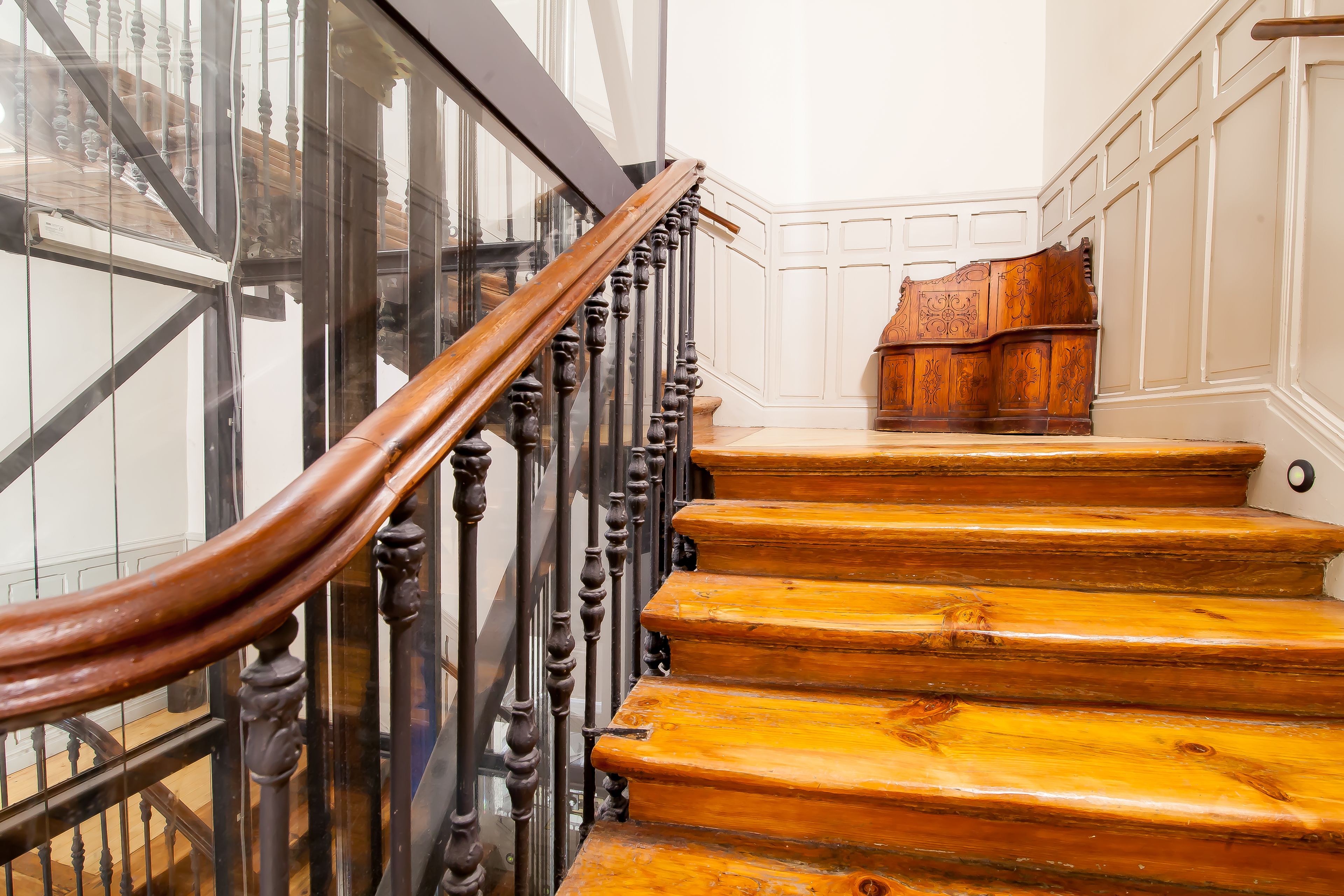 Una escalera de madera con barandilla de cristal y un banco de madera en la parte superior.