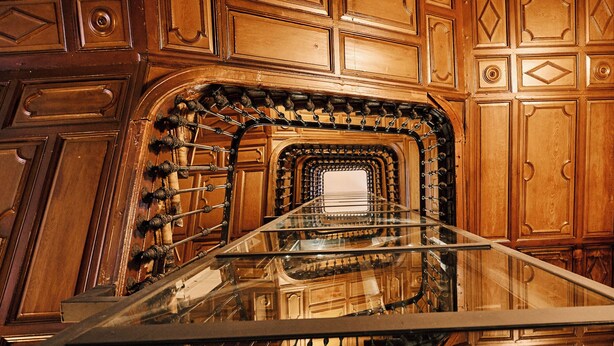 Una imponente escalera de madera con esculturas ornamentales y barandilla de vidrio.