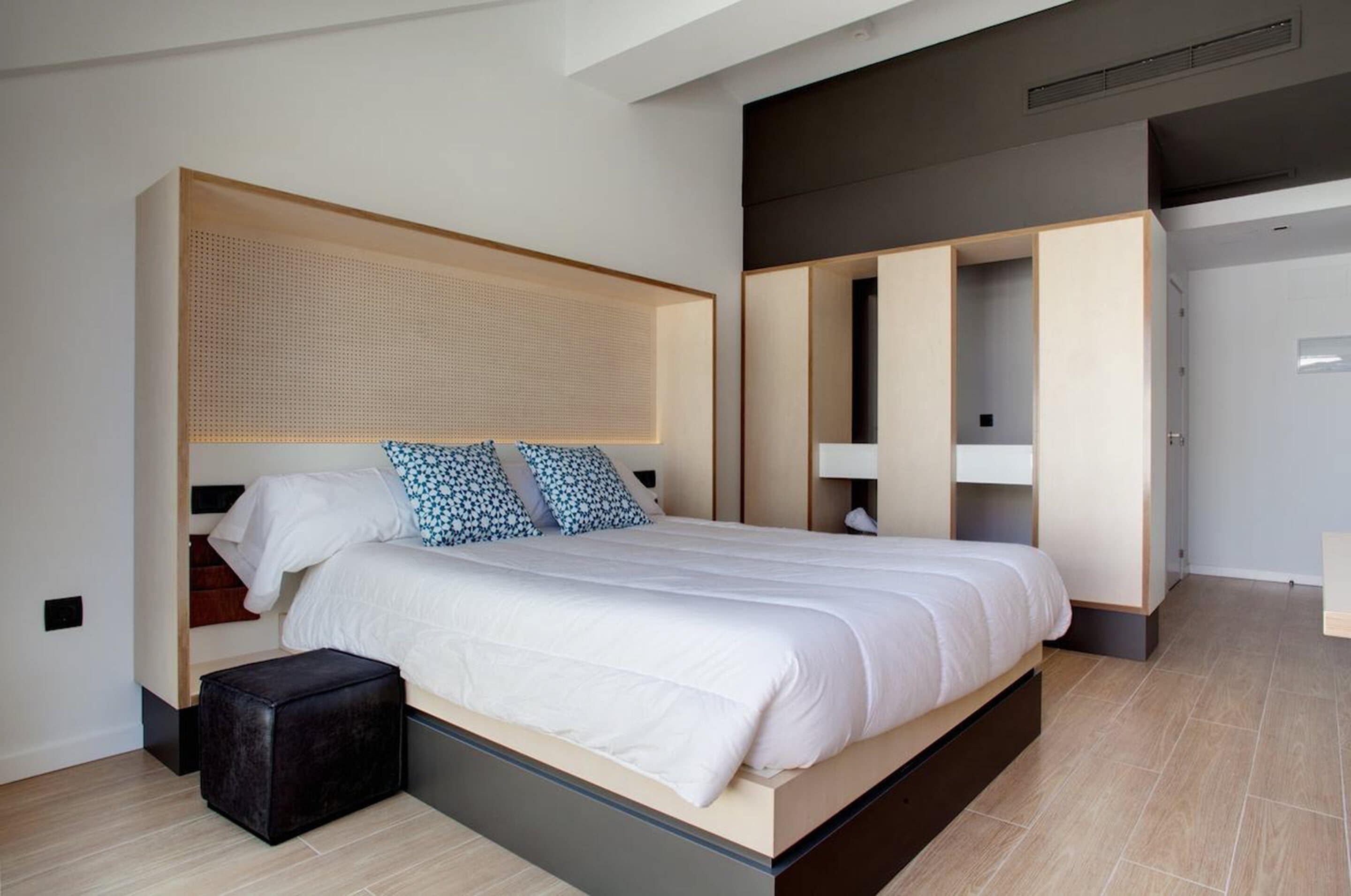 A modern bedroom with a large bed, built-in wardrobe, and a small ottoman.