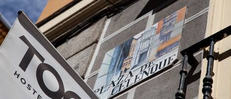 A sign for "TOC Hostel & Suites" with a view of buildings in the background.