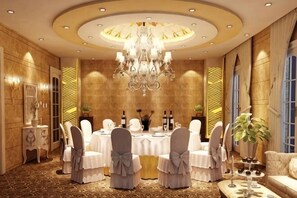 A formal dining room with a round table, white chairs, and a chandelier. - Hua Xi Hotel (Wenshan City)