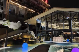 A modern hotel with a glass facade, outdoor seating area, and a pool.