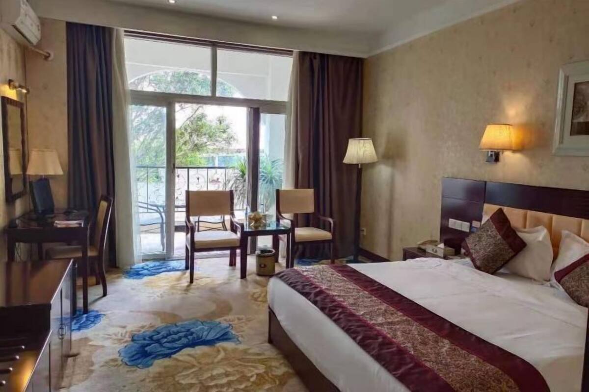 A hotel room with a bed, desk, chair, and a view of the outdoors through a sliding door.