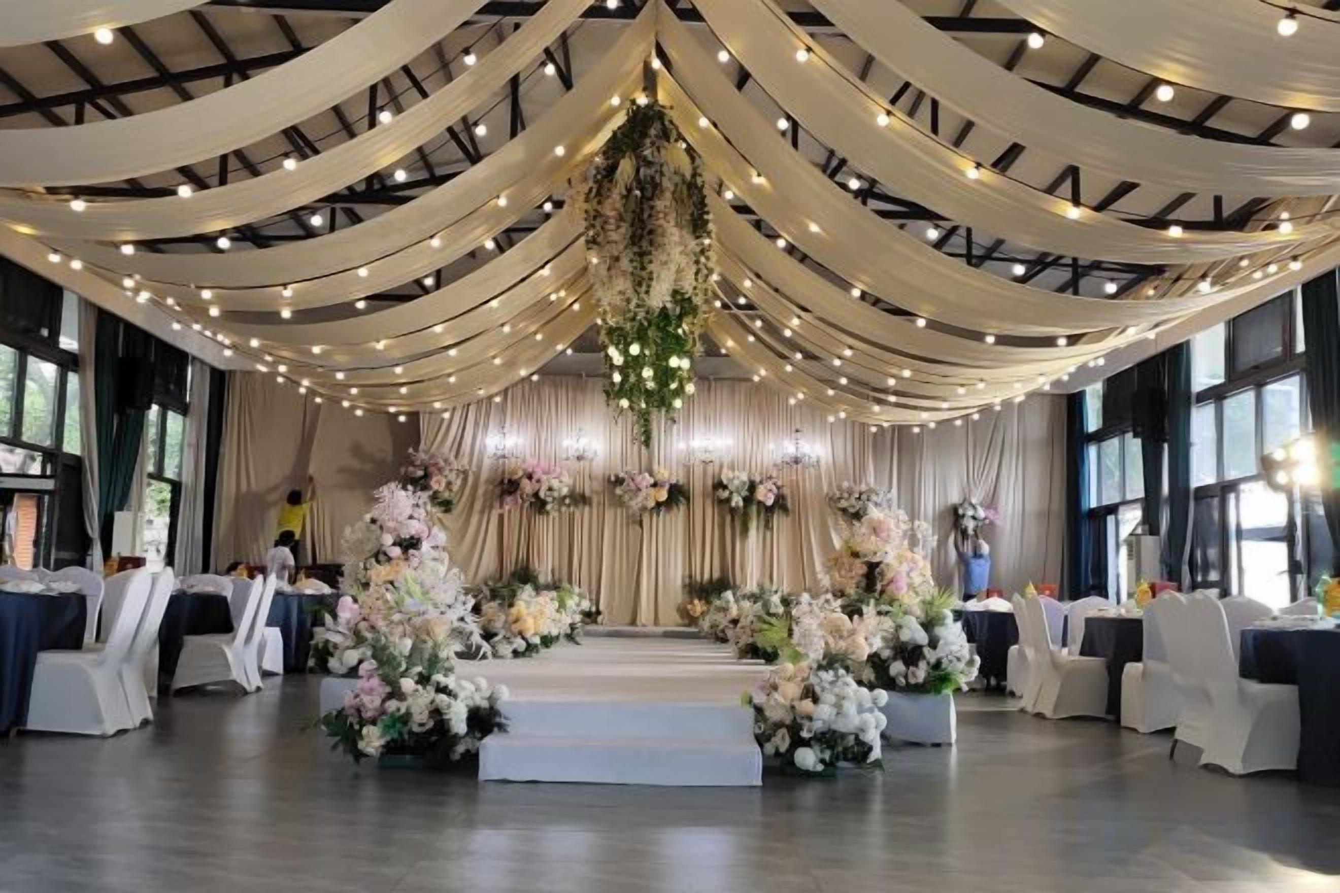 Un espacio interior con escenario, techo decorado con telas y arreglos florales.