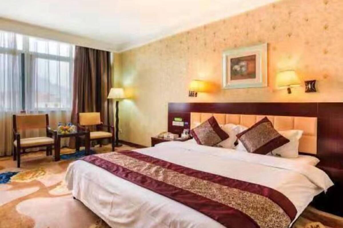 A hotel room with a large bed, a desk with a chair, a nightstand, and a wall-mounted lamp.