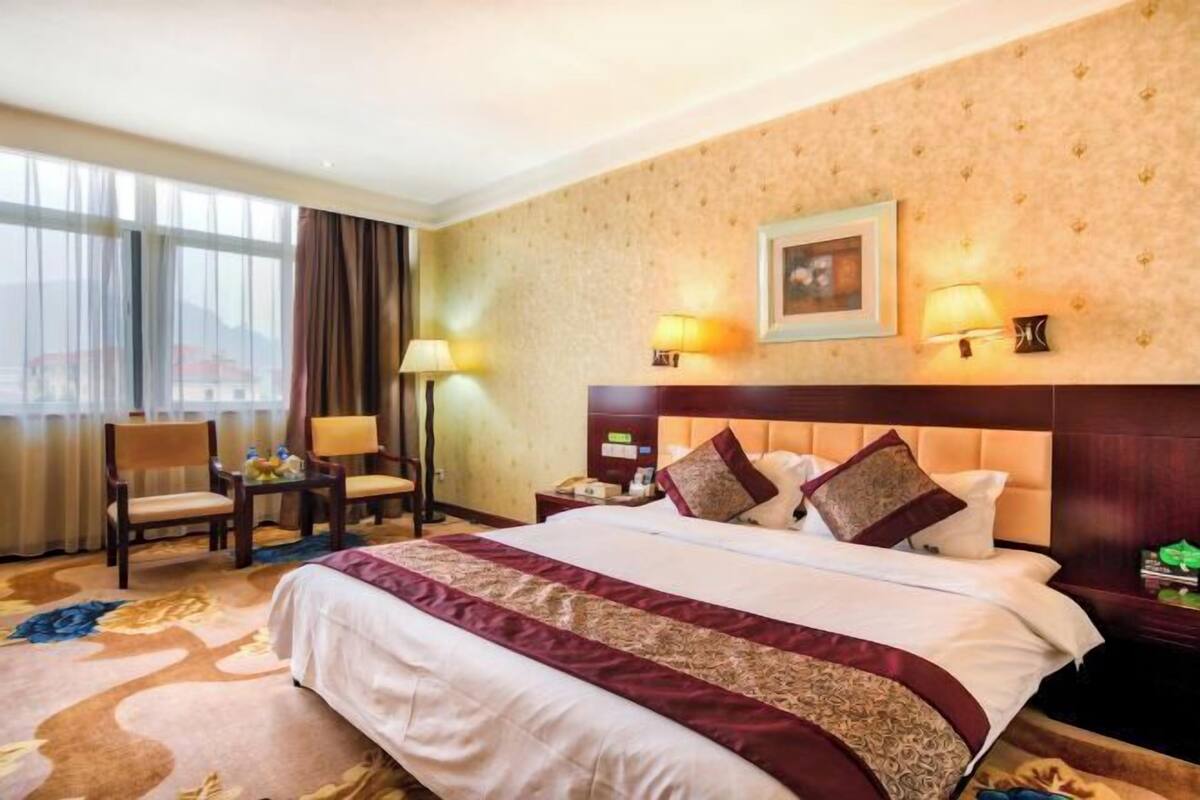 A hotel room with a large bed, two bedside lamps, a nightstand, a chair, and a view of the outdoors.