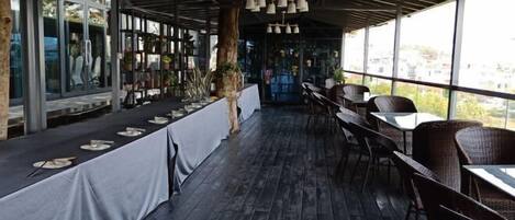 An indoor dining area with a long table set for a meal, surrounded by wicker chairs.