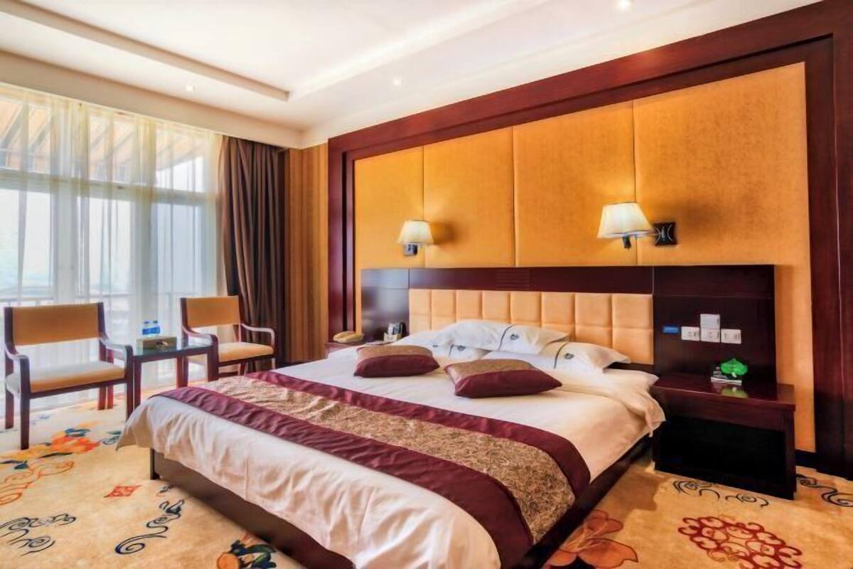 A hotel room with a large bed, two bedside lamps, a nightstand, a chair, and a window with curtains.
