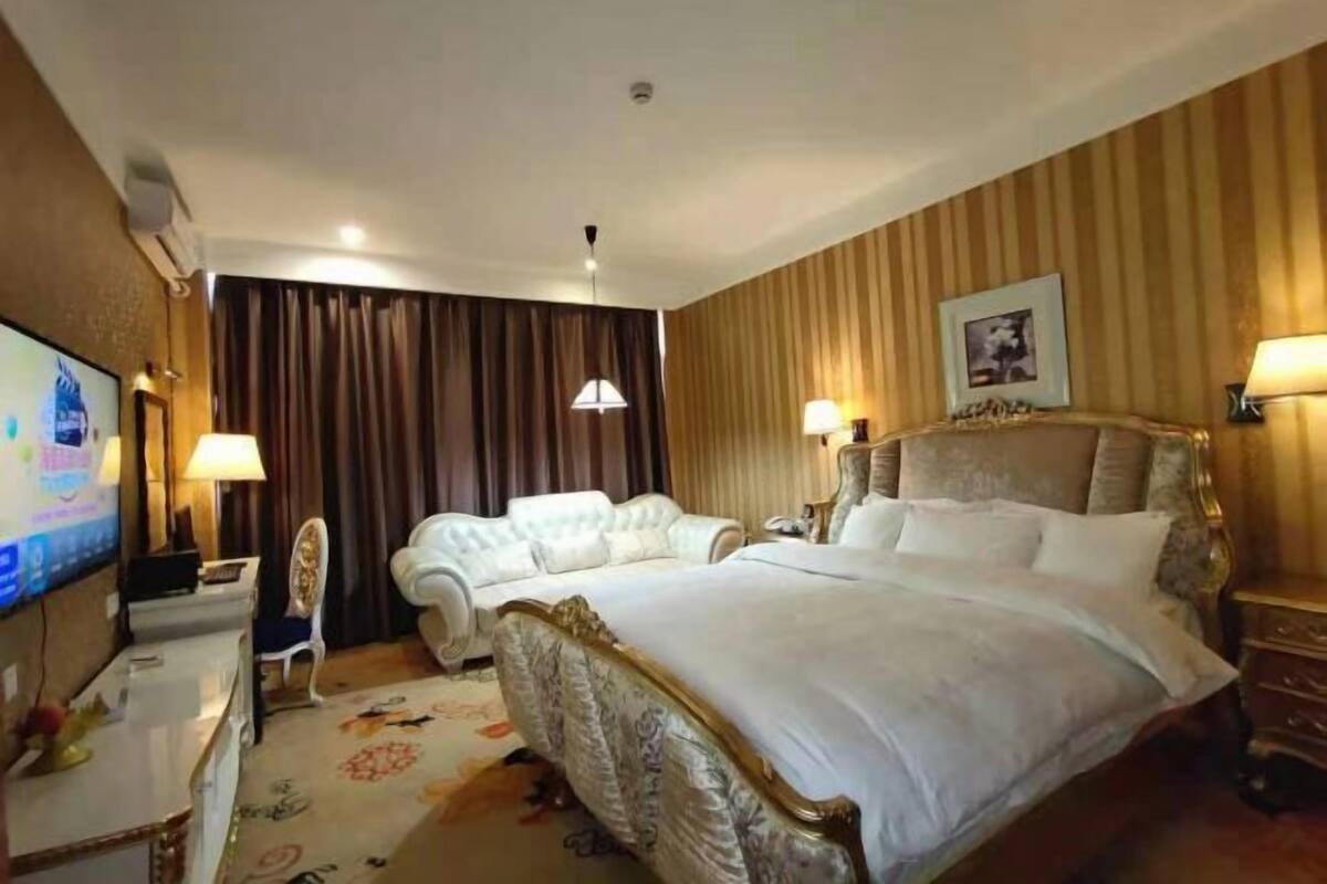 A hotel room with a large bed, a smaller sofa, a TV, and a desk.