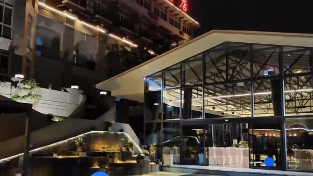 A modern hotel with a glass facade, outdoor seating area, and a water feature. - Hua Xi Hotel (Wenshan City)