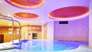 An indoor swimming pool with a tiled floor and walls, surrounded by a circular ceiling design with recessed lighting.