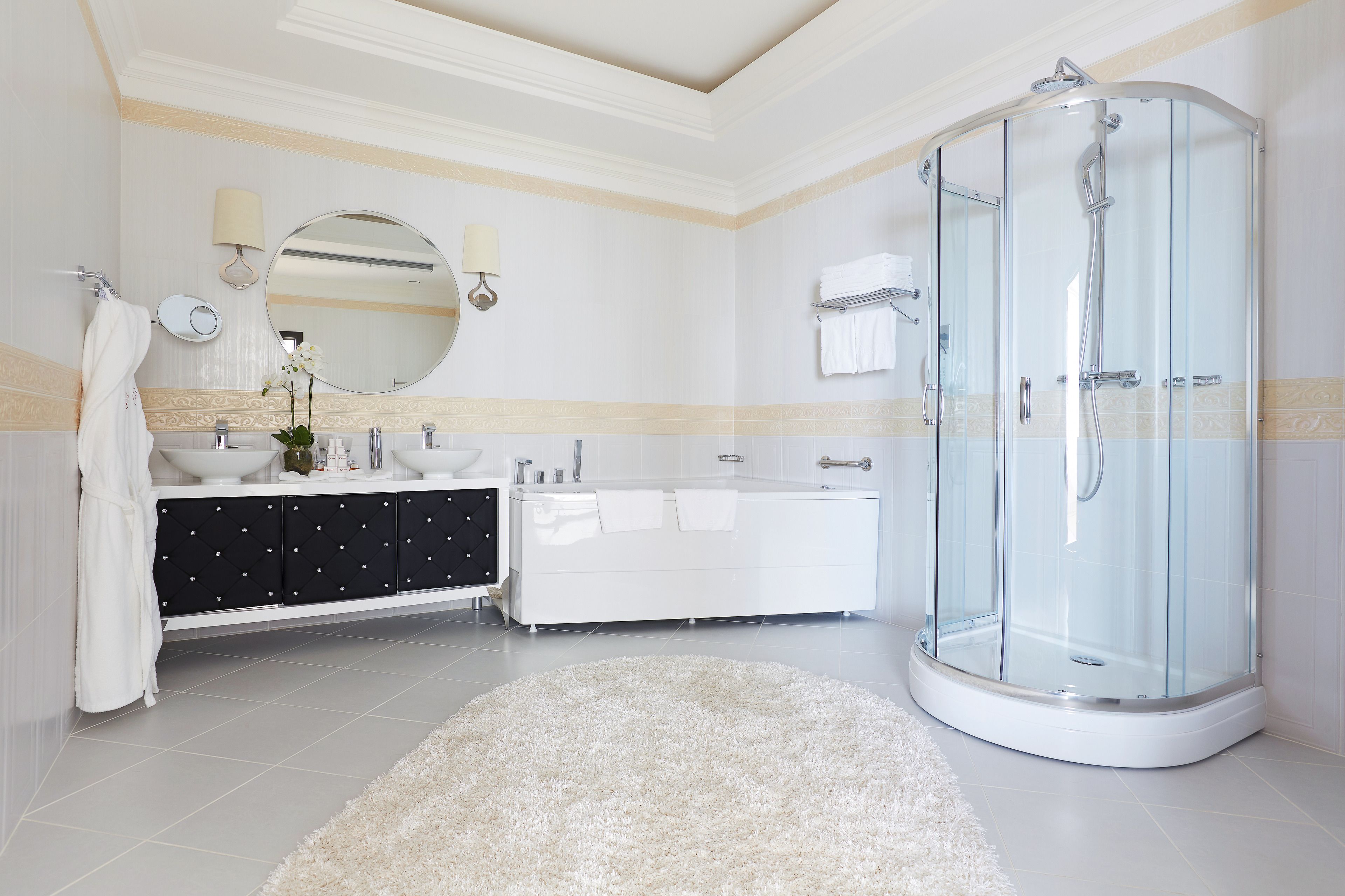 A modern bathroom with a glass-enclosed shower, a white vanity with black drawers, and a round mirror.