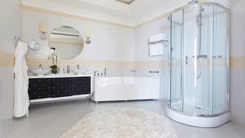 Un baño moderno con ducha de vidrio, tocador blanco con cajones negros y espejo redondo.