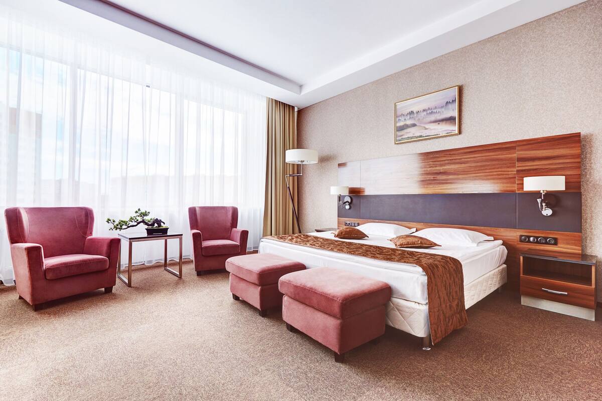 A hotel room with a large bed, two armchairs, a small table, and a nightstand.