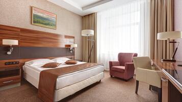 A hotel room with a bed, a desk, a chair, a lamp, and a painting on the wall.