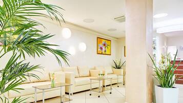 Un vestíbulo de hotel moderno con un sofá color beige, dos mesas con superficie de vidrio y plantas en macetas.