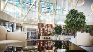 A modern lobby with a glass ceiling, seating areas, and a central plant.