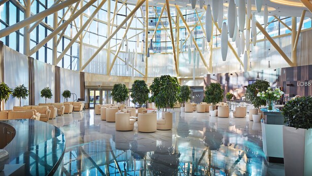 A spacious lobby with a high ceiling, large windows, and modern furniture.