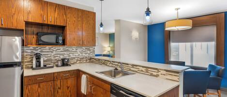 A modern kitchen with wooden cabinets, a built-in microwave, a dishwasher, and a sink. There are pendant lights and a blue accent wall.