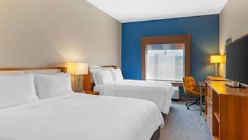 A hotel room with two beds, a desk with a chair, a television, and a window with a view of the outdoors.