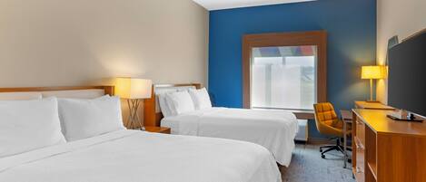 A hotel room with two beds, a desk with a chair, a television, and a window with a view of the outdoors.