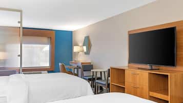 A hotel room with two beds, a desk, a chair, a TV, and a window with blinds.