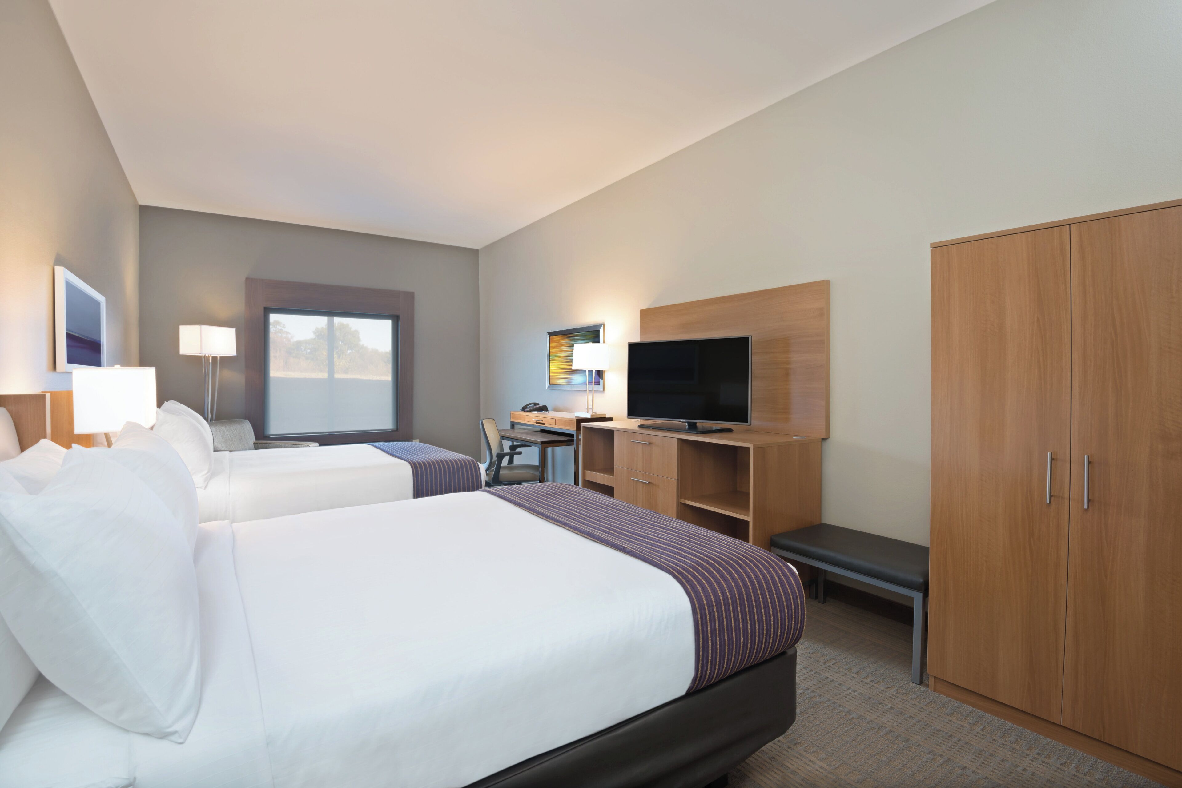A hotel room with two beds, a desk, a television, and a wardrobe.
