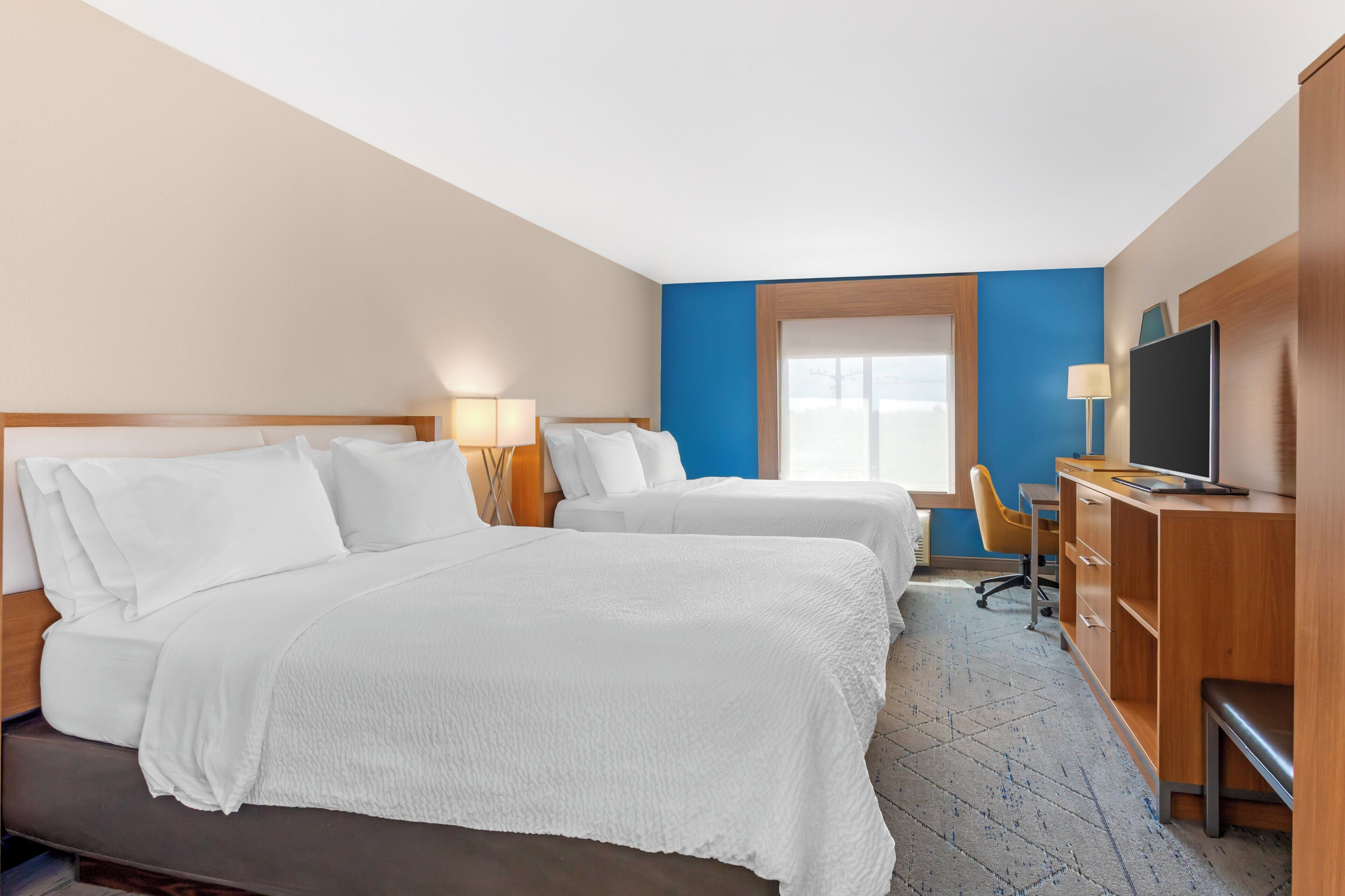 A hotel room with two beds, a desk with a computer, a television, and a window with a view.