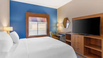 A hotel room with a bed, a desk with a chair, a television, and a window with a view of shipping containers.