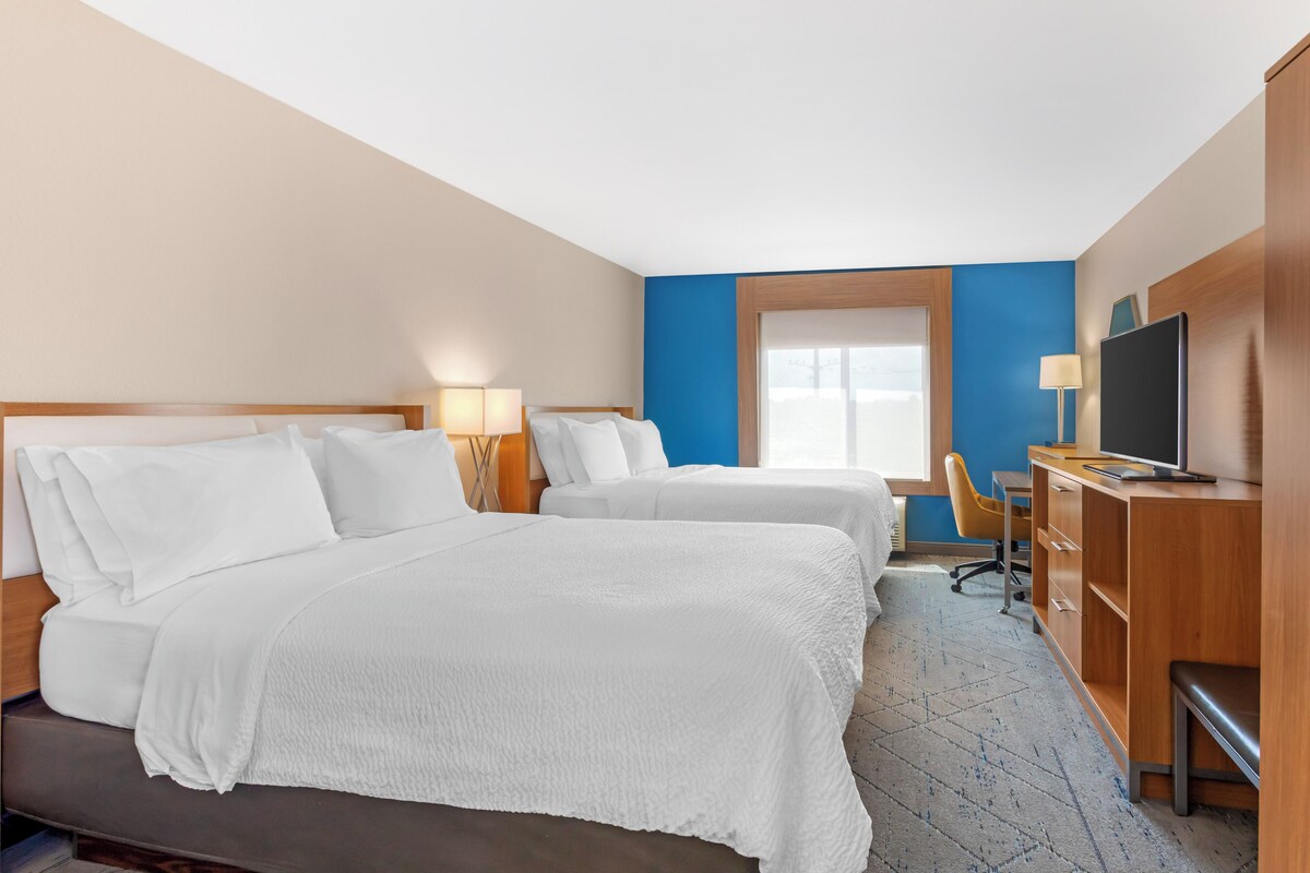 A hotel room with two beds, a desk, a chair, a TV, and a window.