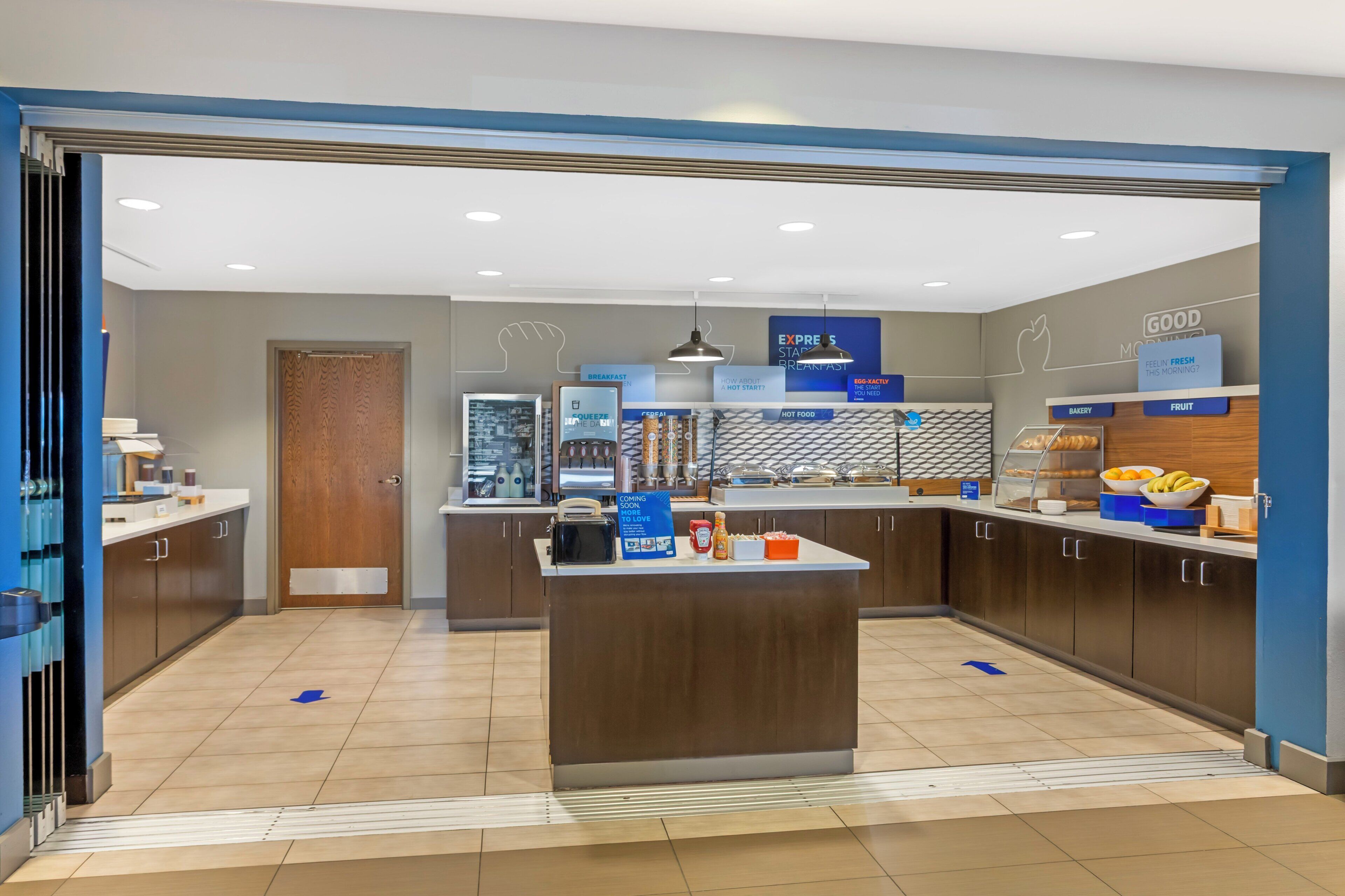 A modern breakfast area with a central island, breakfast bar, and various food stations.