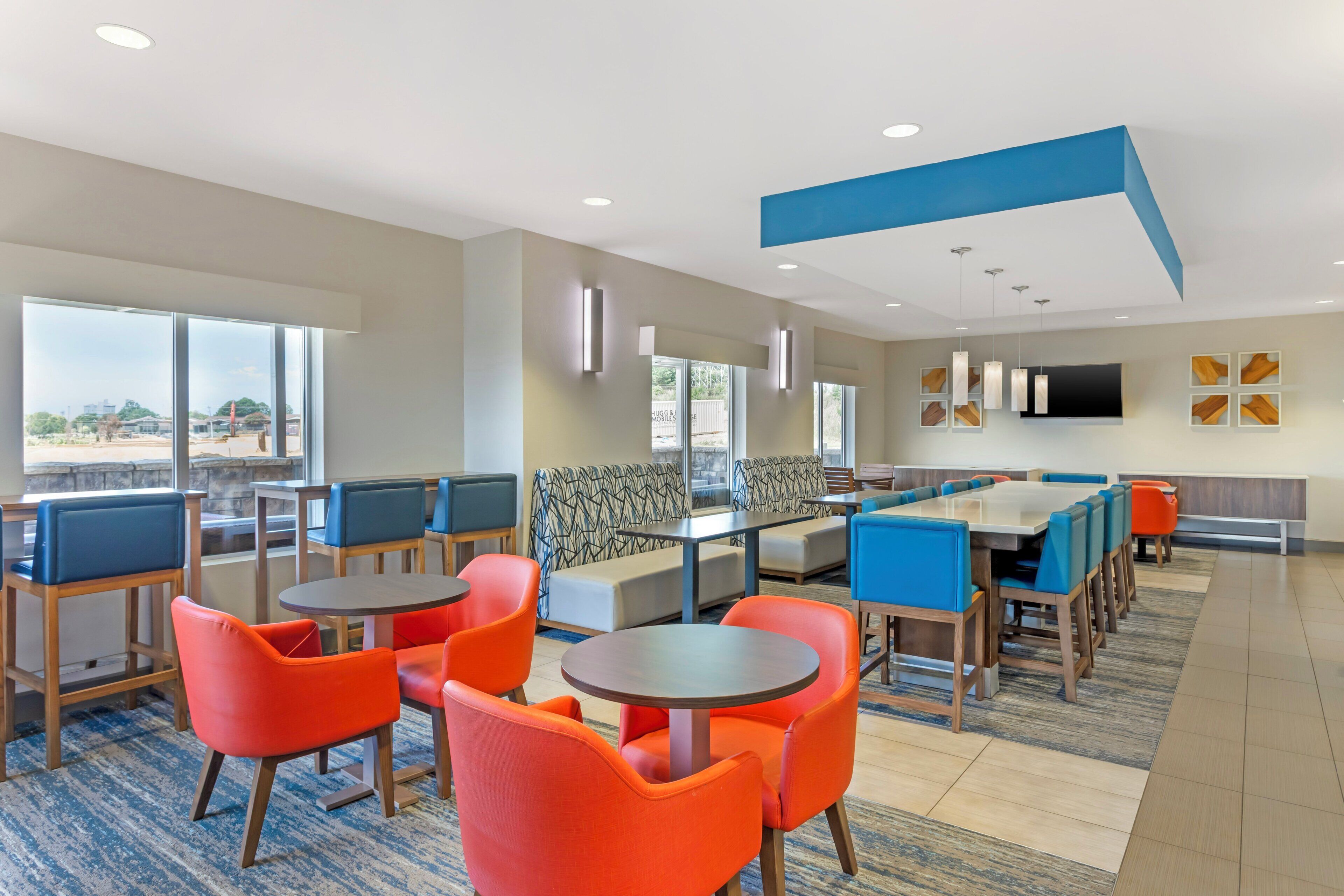 A modern dining area with high tables and chairs, a patterned sofa, and a large window offering a view.