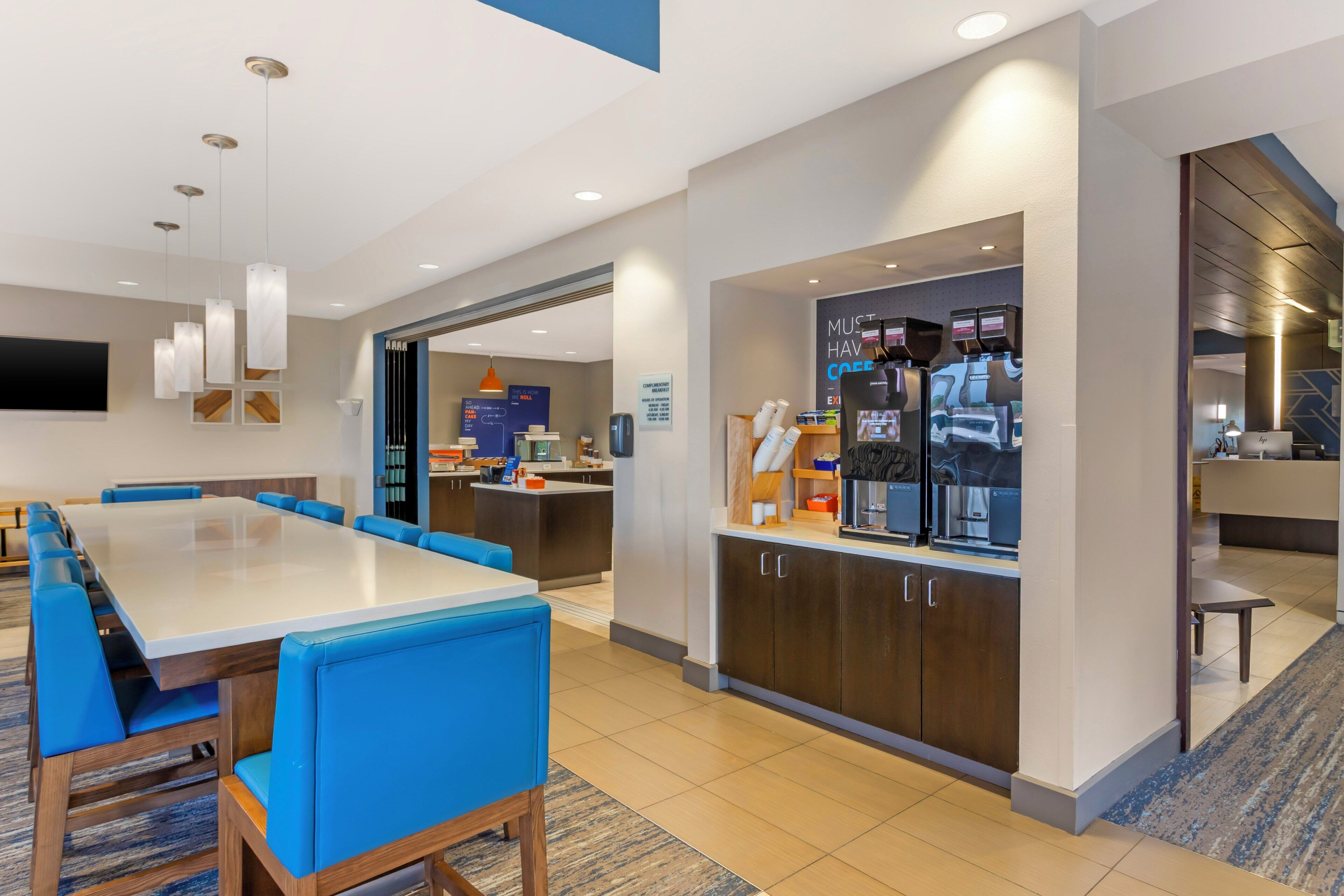 A hotel room with a dining area, kitchenette, and a flat-screen TV mounted on the wall.