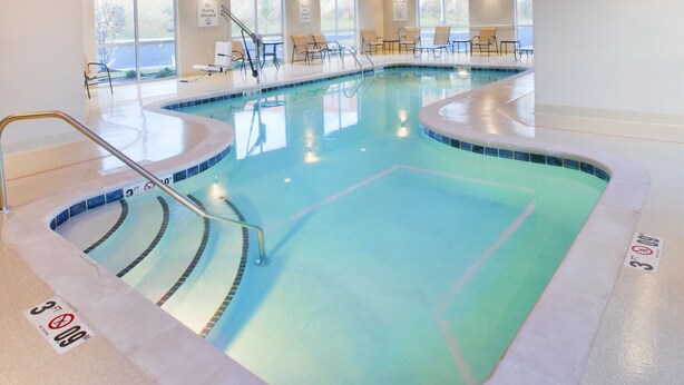 Une piscine au design incurvé, avec un plafond bleu et des éclairages d’ambiance roses.