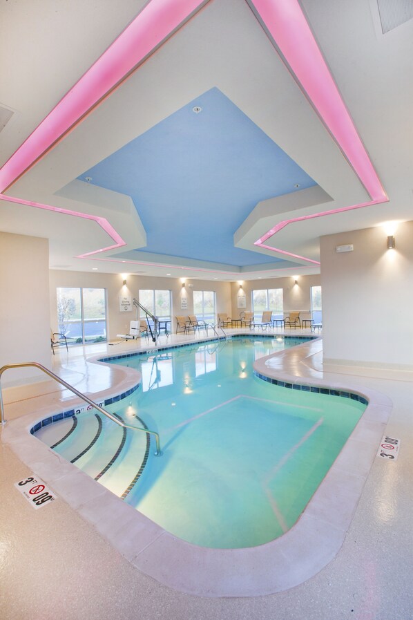 Une piscine au design incurvé, avec un plafond bleu et des éclairages d’ambiance roses.