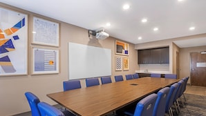 Ett konferensrum med ett långt bord, blå stolar, en whiteboard och inramade konstverk på väggarna.