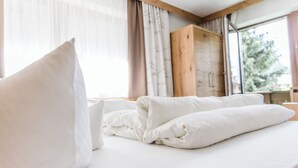 Cama bem arrumada com roupa de cama branca em um quarto com vigas de madeira e janelas amplas.