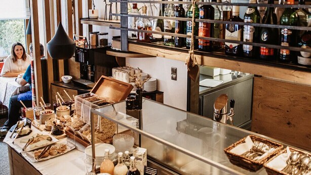 Disposição de buffet com diversos alimentos e acompanhamentos, um espaço para café e um bar com garrafas.